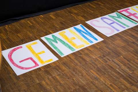 Drei Blätter Papier mit bunten, handgemalten Buchstaben liegen auf einem Holzboden.