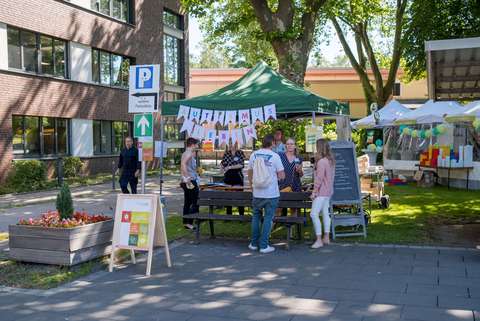 Mehrere Personen stehen und sitzen an einem Infostand mit grünem Pavillon im Freien, darüber hängt eine Girlande mit der Aufschrift „Autismus Leben“.