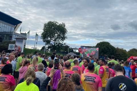 Viele Personen in bunten Sportshirts stehen im Freien vor einer großen Leinwand und einem Stoppschild.
