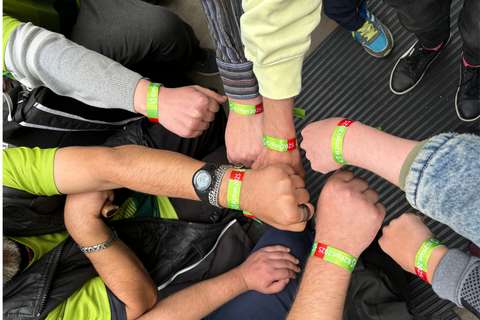 Mehrere Personen halten ihre Fäuste mit grünen Armbändern, auf denen „B2Run 2025“ steht, in der Mitte zusammen.