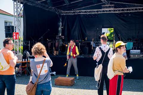 Mehrere Personen stehen vor einer Bühne, auf der eine Person mit buntem Outfit und brennenden Keulen jongliert.