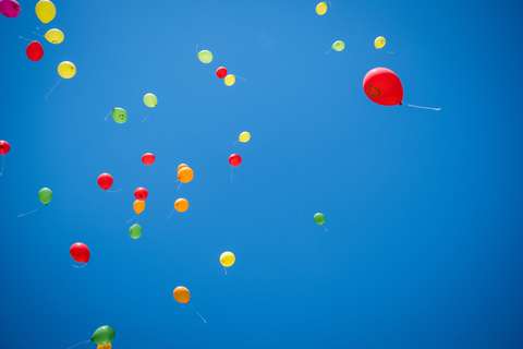 Mehrere bunte Luftballons fliegen am Himmel.