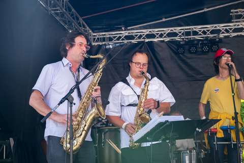 Drei Personen musizieren auf einer Bühne, zwei spielen Saxophon und eine singt in ein Mikrofon.