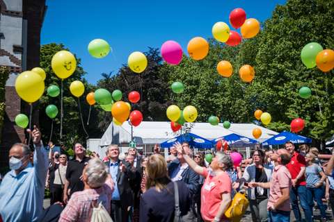 Mehrere Personen stehen im Freien und lassen bunte Luftballons steigen.