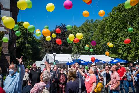 Mehrere Personen stehen im Freien und lassen bunte Luftballons steigen.
