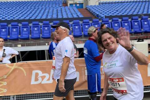 Zwei Personen in Sportkleidung gehen in einem Stadion, eine Person winkt.