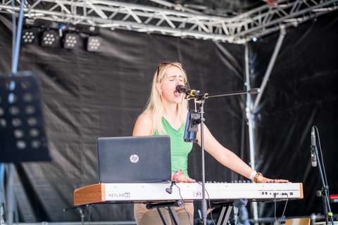 Eine Person spielt Keyboard und singt in ein Mikrofon, vor ihr steht ein Laptop.