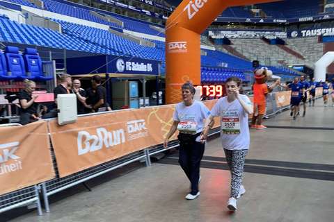 Zwei Personen gehen Hand in Hand durch einen Zielbogen bei einer Laufveranstaltung in einem Stadion.