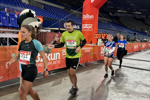 Vier Personen laufen in einem Stadion durch einen roten Zielbogen mit der Aufschrift „B2Run“.