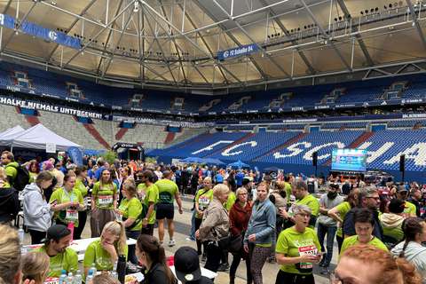 Viele Personen stehen und gehen in einem Stadion, einige tragen grüne T-Shirts mit Startnummern.