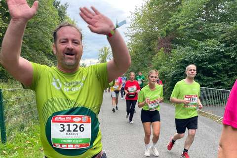 Mehrere Personen laufen auf einer Straße im Freien, einige tragen grüne T-Shirts und Startnummern.