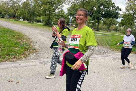 Drei Personen nehmen an einer Laufveranstaltung im Freien teil, zwei tragen grüne Shirts und eine trägt ein weißes Shirt.